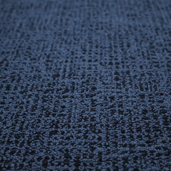 A textured, woven fabric featuring a complex pattern of blue, dark, and navy threads, creating a speckled and mottled appearance.