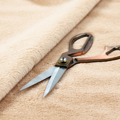 A high-quality faux fur fabric in a warm, sandy beige or light camel hue. The material features a dense, short-pile texture with a soft, uniform grain that gives it a velvety and plush appearance.