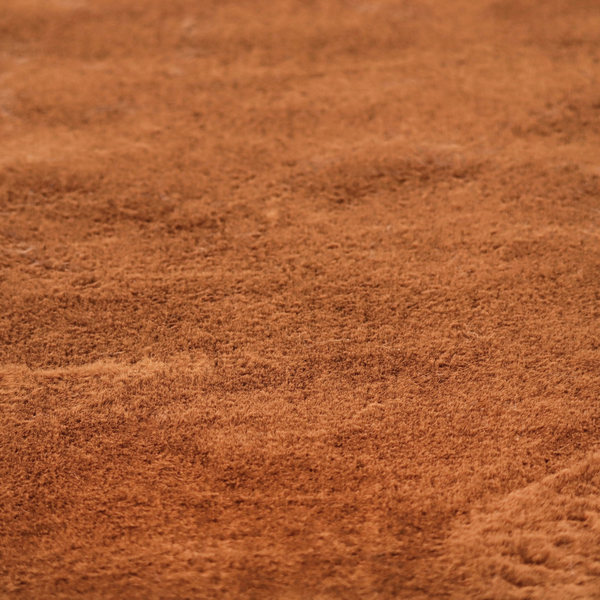 A plush faux fur fabric in a deep, vibrant burnt orange or copper hue. The material displays a dense, short-pile texture that creates a rich, velvet-like appearance. The fibres have a soft, uniform grain that catches the light to reveal warm, glowing undertones, giving the fabric a luxurious sense of depth.
