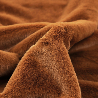 A plush faux fur fabric in a deep, vibrant burnt orange or copper hue. The material displays a dense, short-pile texture that creates a rich, velvet-like appearance. The fibres have a soft, uniform grain that catches the light to reveal warm, glowing undertones, giving the fabric a luxurious sense of depth.