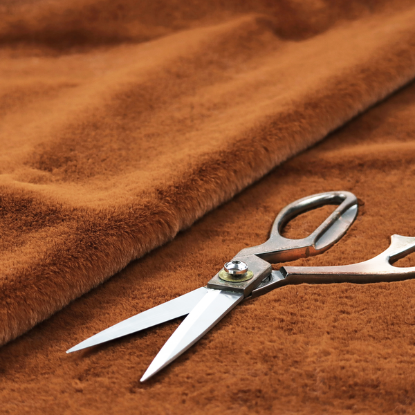 A plush faux fur fabric in a deep, vibrant burnt orange or copper hue. The material displays a dense, short-pile texture that creates a rich, velvet-like appearance. The fibres have a soft, uniform grain that catches the light to reveal warm, glowing undertones, giving the fabric a luxurious sense of depth.