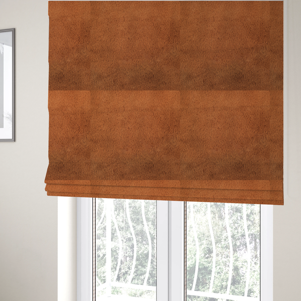 The fabric used to create these Roman blinds is a plush faux fur fabric in a deep, vibrant burnt orange or copper hue. The material displays a dense, short-pile texture that creates a rich, velvet-like appearance. The fibres have a soft, uniform grain that catches the light to reveal warm, glowing undertones, giving the fabric a luxurious sense of depth.