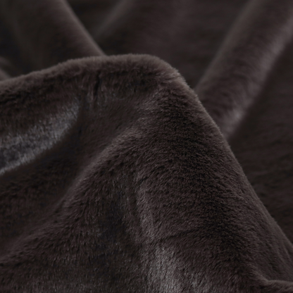 A luxurious faux fur fabric in a deep off-black or charcoal noir shade. The material has an exceptionally dense, short-pile texture that creates a rich, velvet-like surface. The dark fibres catch the light to reveal subtle, cool-toned depth, giving the fabric a sophisticated matte finish.