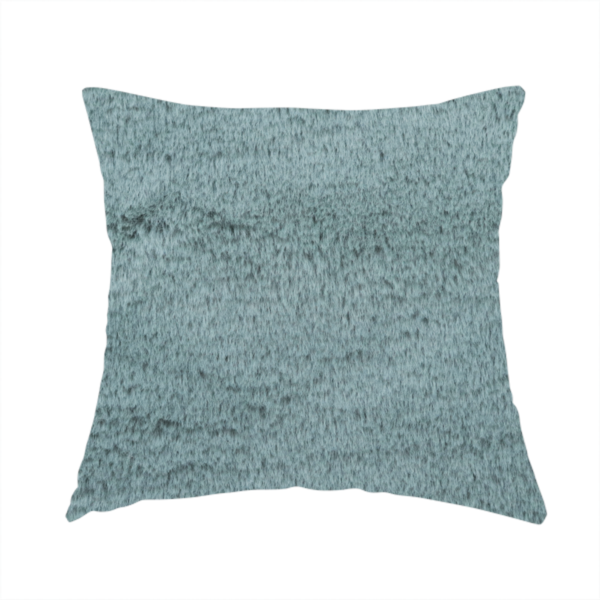 The fabric used to create this handmade cushion is a plush faux fur fabric in a muted dusty teal or slate blue shade. The material has a dense, short-pile texture that creates a soft, uniform surface with a gentle matte sheen. The fibres are tightly packed, showing subtle tonal variations and light shadows that give the fabric a velvety depth.