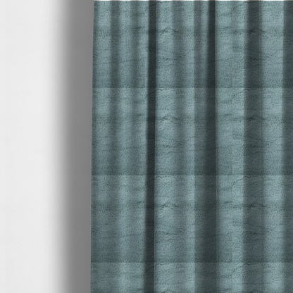 The fabric used to create these made-to-measure curtains is a plush faux fur fabric in a muted dusty teal or slate blue shade. The material has a dense, short-pile texture that creates a soft, uniform surface with a gentle matte sheen. The fibres are tightly packed, showing subtle tonal variations and light shadows that give the fabric a velvety depth.