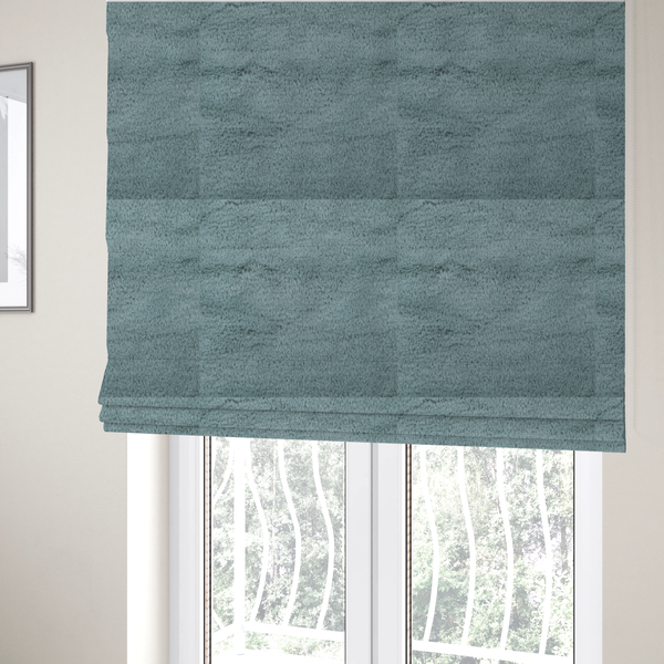The fabric used to create these Roman blinds is a plush faux fur fabric in a muted dusty teal or slate blue shade. The material has a dense, short-pile texture that creates a soft, uniform surface with a gentle matte sheen. The fibres are tightly packed, showing subtle tonal variations and light shadows that give the fabric a velvety depth.