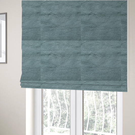 The fabric used to create these Roman blinds is a plush faux fur fabric in a muted dusty teal or slate blue shade. The material has a dense, short-pile texture that creates a soft, uniform surface with a gentle matte sheen. The fibres are tightly packed, showing subtle tonal variations and light shadows that give the fabric a velvety depth.