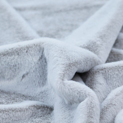A plush faux fur fabric in a bright silver or icy light grey shade. The material has a dense, short-pile texture that creates a soft, uniform surface with a delicate matte sheen. The cool, pale grey fibres are tightly packed, showing subtle light-and-shadow variations that give the fabric a clean, velvety depth.