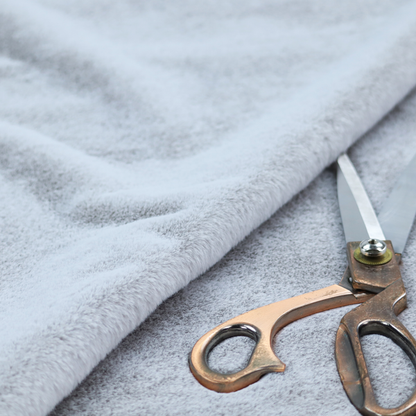 A plush faux fur fabric in a bright silver or icy light grey shade. The material has a dense, short-pile texture that creates a soft, uniform surface with a delicate matte sheen. The cool, pale grey fibres are tightly packed, showing subtle light-and-shadow variations that give the fabric a clean, velvety depth.