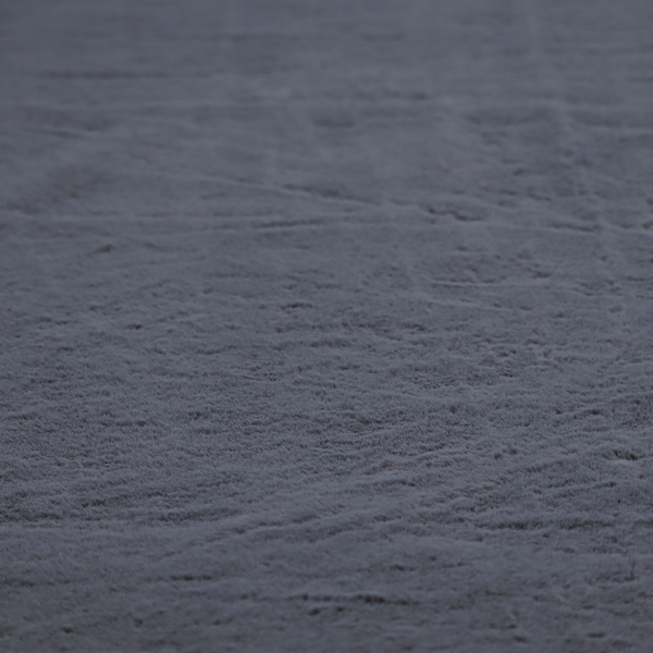 A luxurious faux fur fabric in a deep slate grey or charcoal blue shade. The material features a dense, plush, short-pile texture that creates a soft, uniform surface with a rich matte finish. The tightly packed fibres catch the light to reveal subtle, cool-toned depth and soft shadows, suggesting a velvety and sophisticated hand-feel.