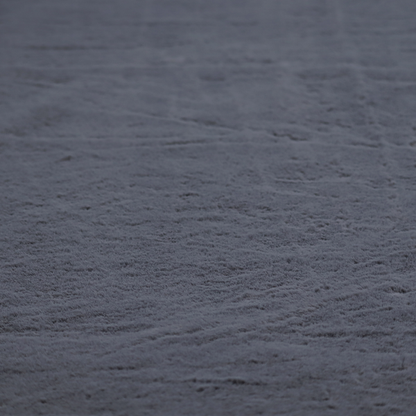 A luxurious faux fur fabric in a deep slate grey or charcoal blue shade. The material features a dense, plush, short-pile texture that creates a soft, uniform surface with a rich matte finish. The tightly packed fibres catch the light to reveal subtle, cool-toned depth and soft shadows, suggesting a velvety and sophisticated hand-feel.