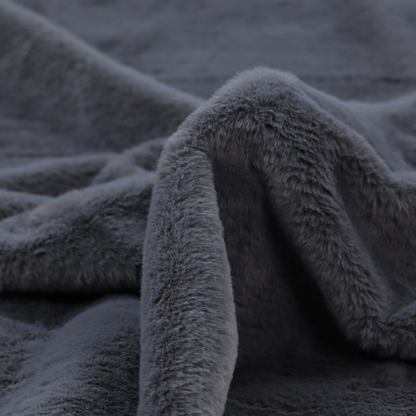 A luxurious faux fur fabric in a deep slate grey or charcoal blue shade. The material features a dense, plush, short-pile texture that creates a soft, uniform surface with a rich matte finish. The tightly packed fibres catch the light to reveal subtle, cool-toned depth and soft shadows, suggesting a velvety and sophisticated hand-feel.