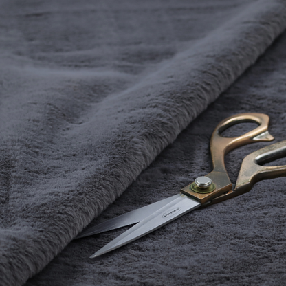 A luxurious faux fur fabric in a deep slate grey or charcoal blue shade. The material features a dense, plush, short-pile texture that creates a soft, uniform surface with a rich matte finish. The tightly packed fibres catch the light to reveal subtle, cool-toned depth and soft shadows, suggesting a velvety and sophisticated hand-feel.