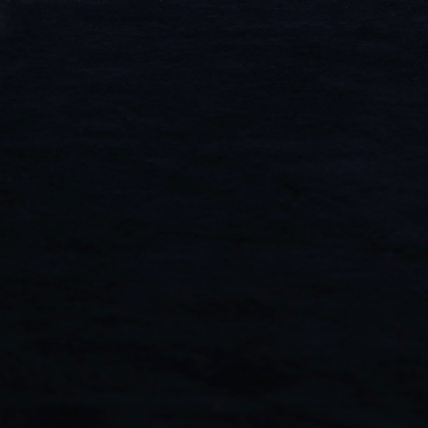 A luxurious faux fur fabric in a solid, true jet black. The material showcases an exceptionally dense, short-pile texture with a soft, uniform grain that creates a deep matte finish. Because of its high density, the fabric absorbs light significantly, resulting in a rich, velvety appearance with minimal sheen.