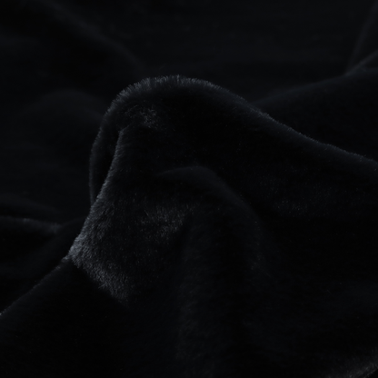 A luxurious faux fur fabric in a solid, true jet black. The material showcases an exceptionally dense, short-pile texture with a soft, uniform grain that creates a deep matte finish. Because of its high density, the fabric absorbs light significantly, resulting in a rich, velvety appearance with minimal sheen.