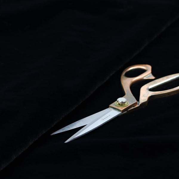 A luxurious faux fur fabric in a solid, true jet black. The material showcases an exceptionally dense, short-pile texture with a soft, uniform grain that creates a deep matte finish. Because of its high density, the fabric absorbs light significantly, resulting in a rich, velvety appearance with minimal sheen.