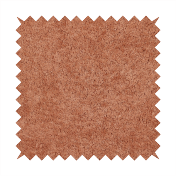 A soft, textured fabric in a warm, muted terracotta or rust shade. The surface features a dense, uniform, and plush pile, characteristic of thick fleece or absorbent terry cloth material.