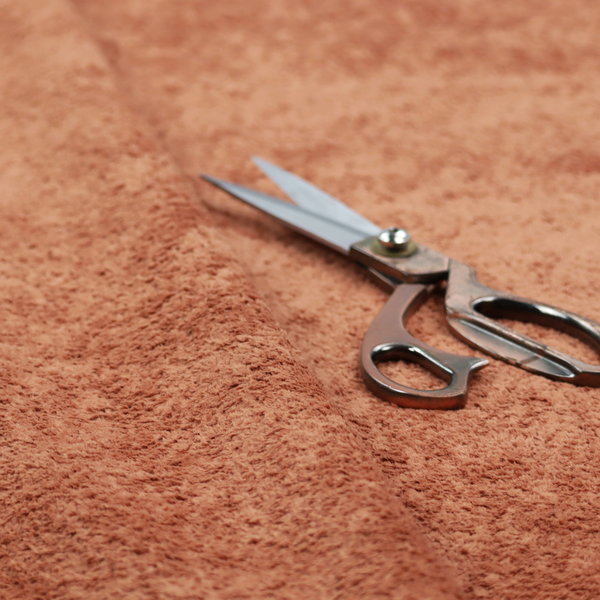 A soft, textured fabric in a warm, muted terracotta or rust shade. The surface features a dense, uniform, and plush pile, characteristic of thick fleece or absorbent terry cloth material.