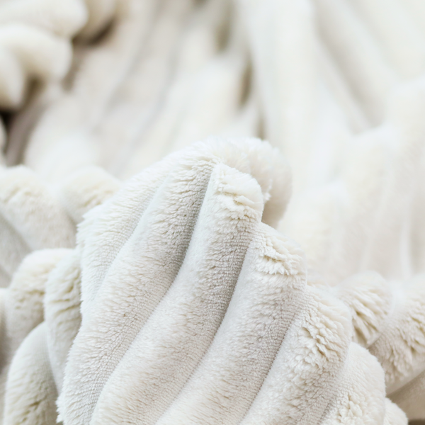 A cream-coloured textile featuring a repeating, vertical ribbed pattern. The fabric alternates between wide, soft, faux-fur-like plush bands and narrow, smooth, flat channels.