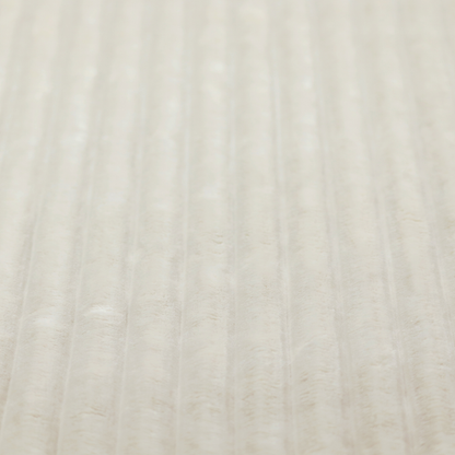 A detailed view of a light beige or cream-coloured textile featuring a repeating, vertical channel-tufted pattern. The material alternates between soft, high-pile plush bands and thin, compressed vertical lines.