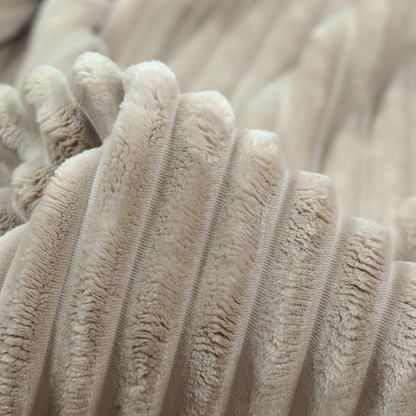 A warm, beige-toned textile featuring a repeating, vertical channel-tufted pattern. The fabric alternates between thick, high-pile plush bands and thin, compressed vertical channels.