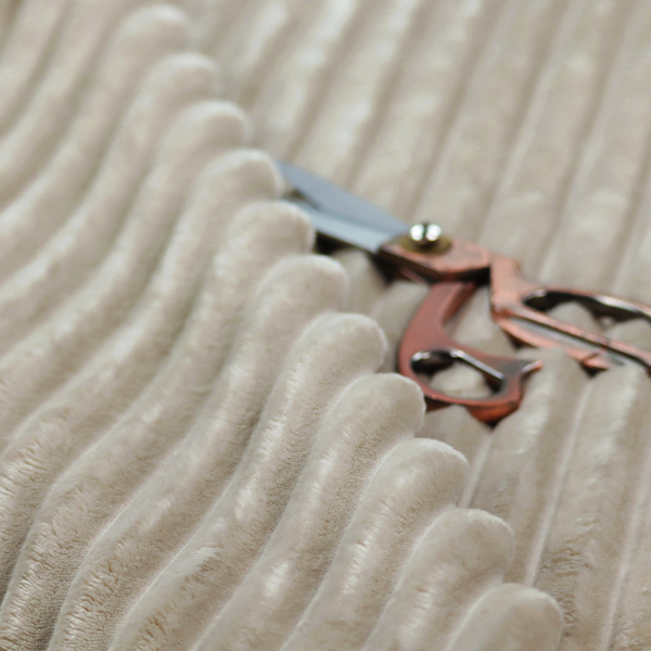 A warm, beige-toned textile featuring a repeating, vertical channel-tufted pattern. The fabric alternates between thick, high-pile plush bands and thin, compressed vertical channels.