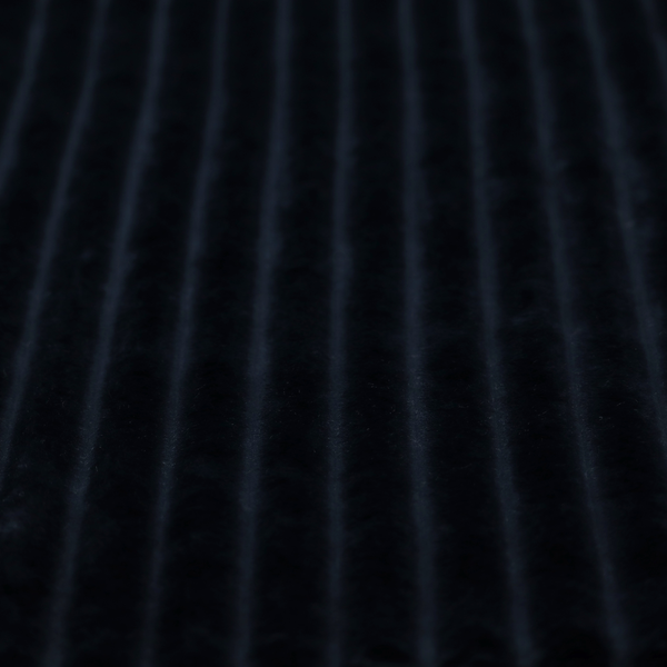 A deep black textile featuring a repeating, vertical channel-tufted pattern. The fabric alternates between thick, high-pile plush bands and thin, compressed vertical channels.
