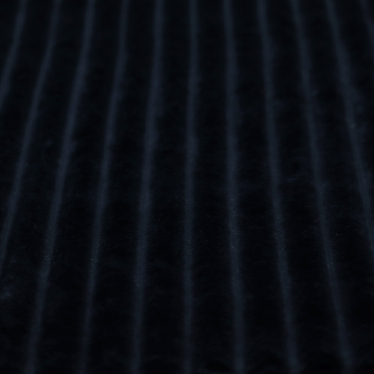A deep black textile featuring a repeating, vertical channel-tufted pattern. The fabric alternates between thick, high-pile plush bands and thin, compressed vertical channels.