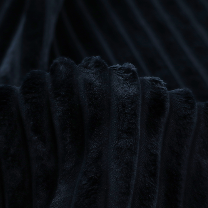 A deep black textile featuring a repeating, vertical channel-tufted pattern. The fabric alternates between thick, high-pile plush bands and thin, compressed vertical channels.