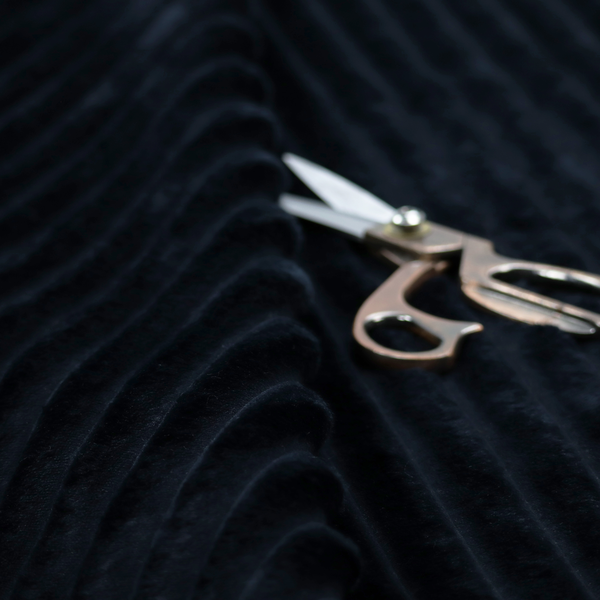 A deep black textile featuring a repeating, vertical channel-tufted pattern. The fabric alternates between thick, high-pile plush bands and thin, compressed vertical channels.