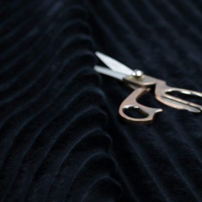 A deep black textile featuring a repeating, vertical channel-tufted pattern. The fabric alternates between thick, high-pile plush bands and thin, compressed vertical channels.