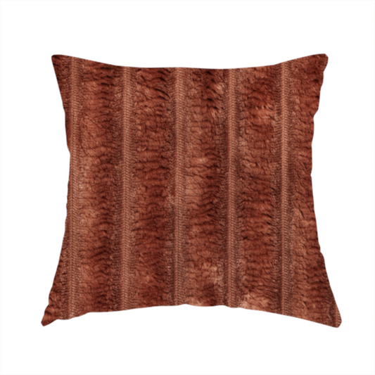 The fabric used to create this handmade cushion is a orange rust, vertically ribbed, channel-tufted plush fabric with a soft, fuzzy texture.
