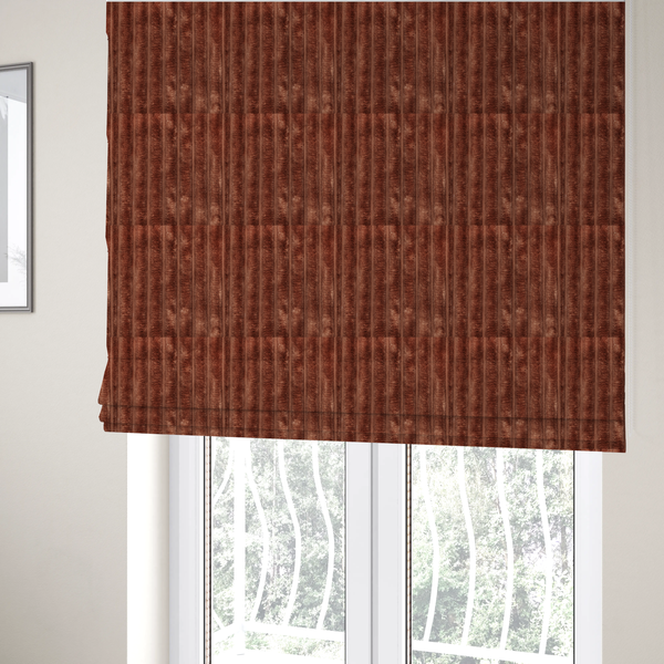 The fabric used to create these Roman blinds is a orange rust, vertically ribbed, channel-tufted plush fabric with a soft, fuzzy texture.