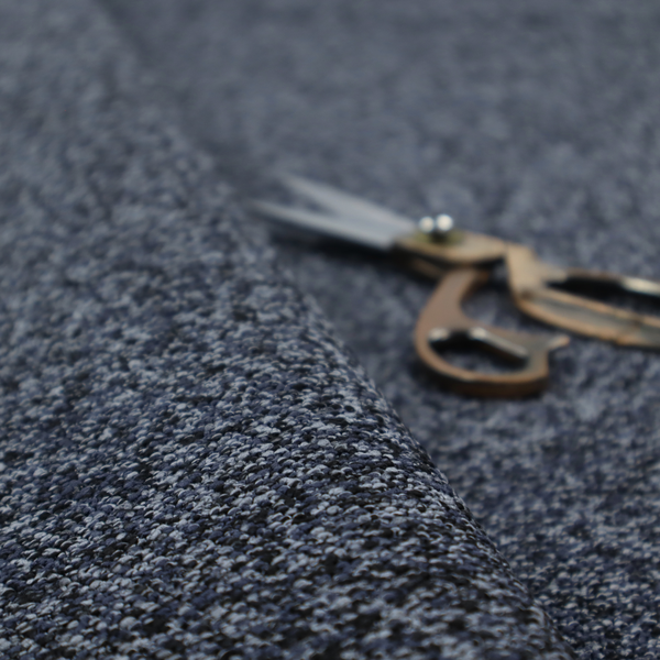 A textured fabric surface. The material features a dense, nubby appearance with a speckled, multi-tonal colour palette of dark navy blue, charcoal, and light grey fibres, characteristic of heavy-duty carpeting or upholstery.