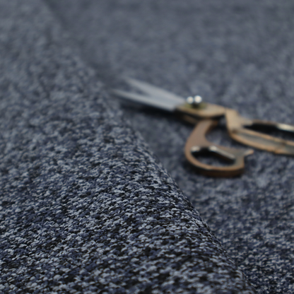 A textured fabric surface. The material features a dense, nubby appearance with a speckled, multi-tonal colour palette of dark navy blue, charcoal, and light grey fibres, characteristic of heavy-duty carpeting or upholstery.