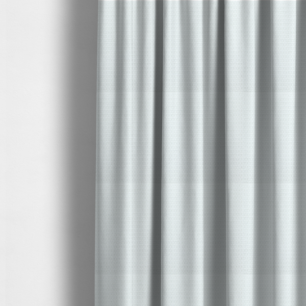 The fabric used to create these made-to-measure curtains is a white, textured fabric with a dense, rhythmic pattern. The material features a honeycomb or waffle-weave structure, where small, uniform raised circles create a grid-like tactile surface. The colour is a bright, cool-toned white, and the subtle shadows within the weave give the fabric a soft, multidimensional appearance.