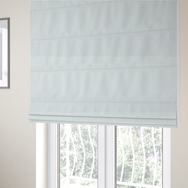 The fabric used to create these Roman blinds is a white, textured fabric with a dense, rhythmic pattern. The material features a honeycomb or waffle-weave structure, where small, uniform raised circles create a grid-like tactile surface. The colour is a bright, cool-toned white, and the subtle shadows within the weave give the fabric a soft, multidimensional appearance.