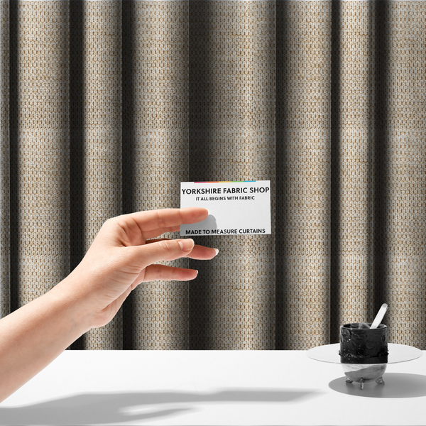 The fabric used to create these made-to-measure curtains is a textured, multi-tonal beige and tan fabric. The material features a tight, intricate weave that creates a pebbled or "seed stitch" appearance. The colour is a warm sand or wheat palette, achieved by interlacing light cream threads with darker tan or straw-coloured fibres, giving the fabric a rich, organic depth.