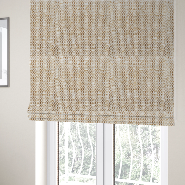 The fabric used to create these Roman blinds is a textured, multi-tonal beige and tan fabric. The material features a tight, intricate weave that creates a pebbled or "seed stitch" appearance. The colour is a warm sand or wheat palette, achieved by interlacing light cream threads with darker tan or straw-coloured fibres, giving the fabric a rich, organic depth.