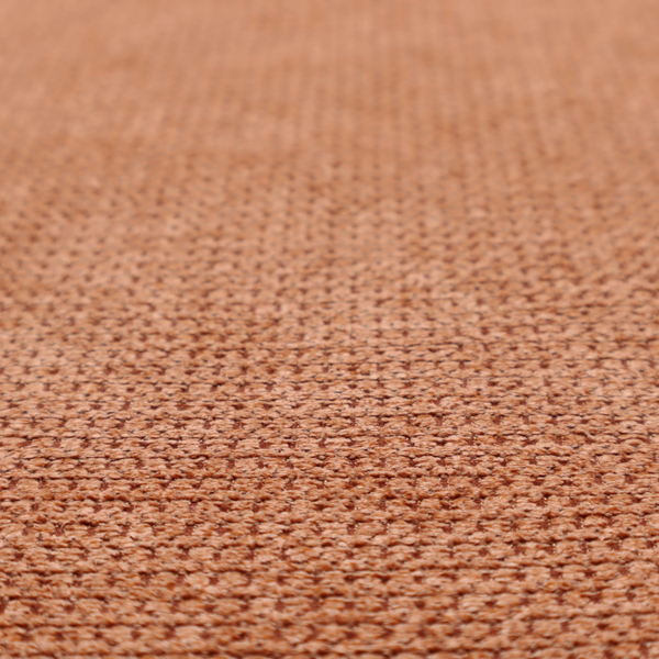 A textured, deep terracotta or burnt orange fabric. This material features a dense, uniform weave with a tactile, honeycombed surface. The colour is a rich, saturated earth tone, created by tightly interlacing copper-coloured threads that catch the light, giving the fabric a subtle, warm glow and a complex, pebbled depth.