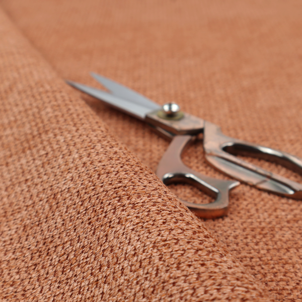 A textured, deep terracotta or burnt orange fabric. This material features a dense, uniform weave with a tactile, honeycombed surface. The colour is a rich, saturated earth tone, created by tightly interlacing copper-coloured threads that catch the light, giving the fabric a subtle, warm glow and a complex, pebbled depth.