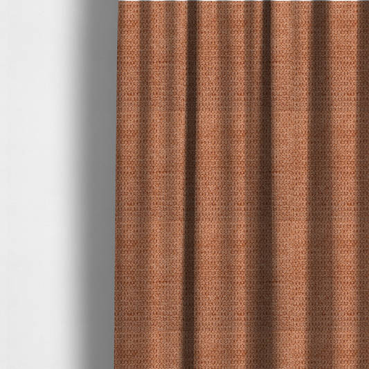 The fabric used to create these made-to-measure curtains is a textured, deep terracotta or burnt orange fabric. This material features a dense, uniform weave with a tactile, honeycombed surface. The colour is a rich, saturated earth tone, created by tightly interlacing copper-coloured threads that catch the light, giving the fabric a subtle, warm glow and a complex, pebbled depth.