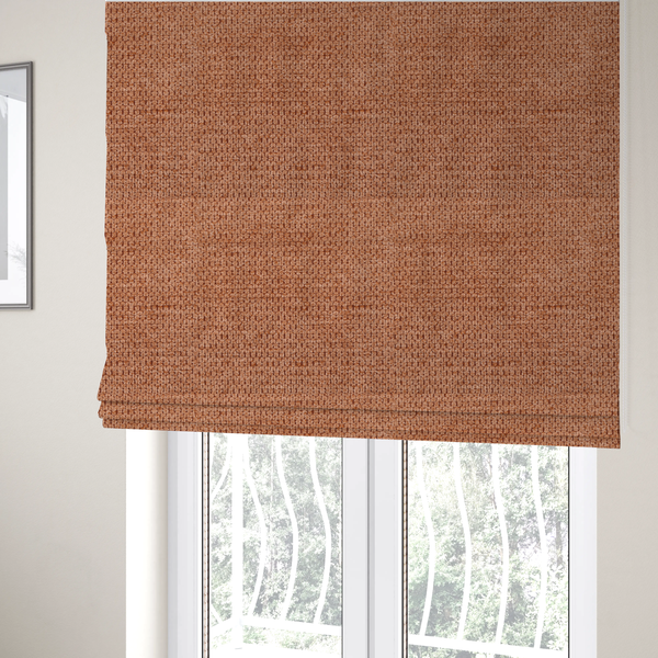 The fabric used to create these Roman blinds is a textured, deep terracotta or burnt orange fabric. This material features a dense, uniform weave with a tactile, honeycombed surface. The colour is a rich, saturated earth tone, created by tightly interlacing copper-coloured threads that catch the light, giving the fabric a subtle, warm glow and a complex, pebbled depth.