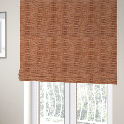 The fabric used to create these Roman blinds is a textured, deep terracotta or burnt orange fabric. This material features a dense, uniform weave with a tactile, honeycombed surface. The colour is a rich, saturated earth tone, created by tightly interlacing copper-coloured threads that catch the light, giving the fabric a subtle, warm glow and a complex, pebbled depth.