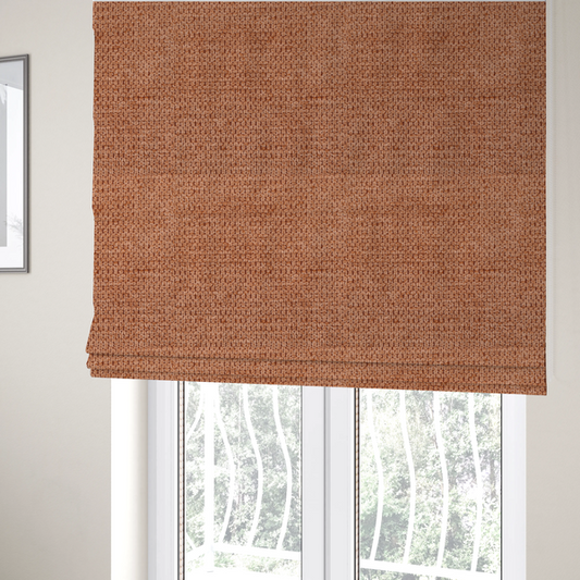 The fabric used to create these Roman blinds is a textured, deep terracotta or burnt orange fabric. This material features a dense, uniform weave with a tactile, honeycombed surface. The colour is a rich, saturated earth tone, created by tightly interlacing copper-coloured threads that catch the light, giving the fabric a subtle, warm glow and a complex, pebbled depth.