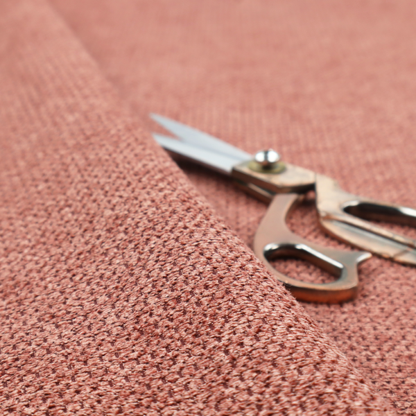 A textured fabric in a muted rose or dusty clay tone. The material features a dense, rhythmic weave with a tactile, pebbled surface. The colour is a sophisticated, warm mauve, created by interlacing deep pinkish-brown threads with lighter rose fibres, giving it a weathered, multi-dimensional look.