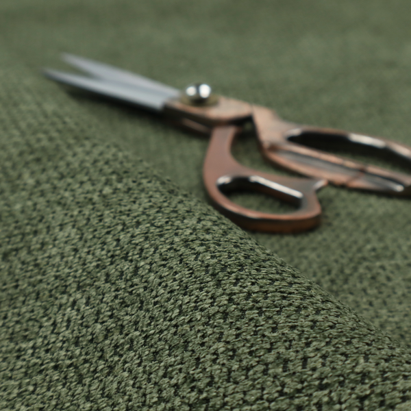 A textured fabric in a deep forest or moss green tone. The material features a dense, rhythmic weave with a prominent tactile surface. The colour is a rich, moody evergreen, achieved by interlacing dark green threads with subtle black or charcoal base fibres, creating a sophisticated, shadowed depth throughout the honeycomb-like pattern.