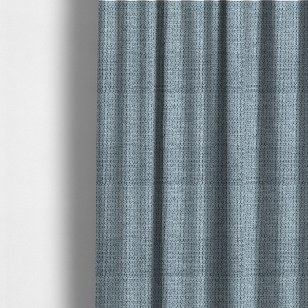 The fabric used to create these made-to-measure curtains is a textured fabric in a light steel or airy powder blue. This material features a dense, rhythmic weave with a tactile, honeycomb-like surface. The colour is a cool, soft frost blue, achieved by interlacing pale blue threads with darker grey base fibres, resulting in a weathered, multidimensional look that feels light yet substantial.