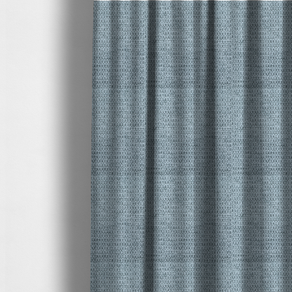 The fabric used to create these made-to-measure curtains is a textured fabric in a light steel or airy powder blue. This material features a dense, rhythmic weave with a tactile, honeycomb-like surface. The colour is a cool, soft frost blue, achieved by interlacing pale blue threads with darker grey base fibres, resulting in a weathered, multidimensional look that feels light yet substantial.