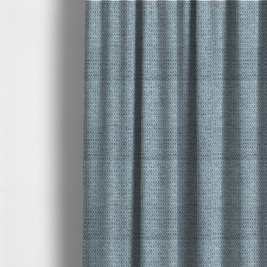 The fabric used to create these made-to-measure curtains is a textured fabric in a light steel or airy powder blue. This material features a dense, rhythmic weave with a tactile, honeycomb-like surface. The colour is a cool, soft frost blue, achieved by interlacing pale blue threads with darker grey base fibres, resulting in a weathered, multidimensional look that feels light yet substantial.